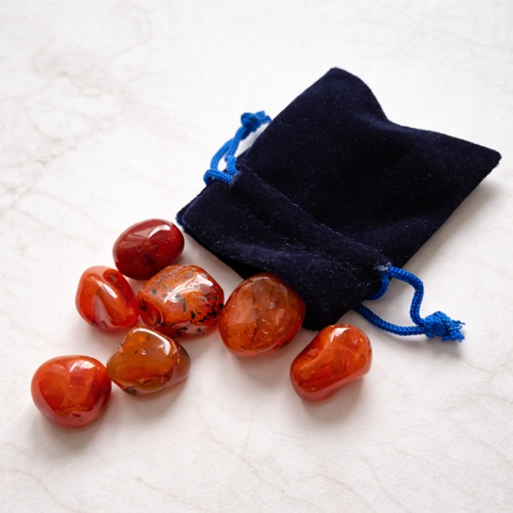 Karneol Trommelsteine Set mit Samtbeutel auf hellem Marmorhintergrund